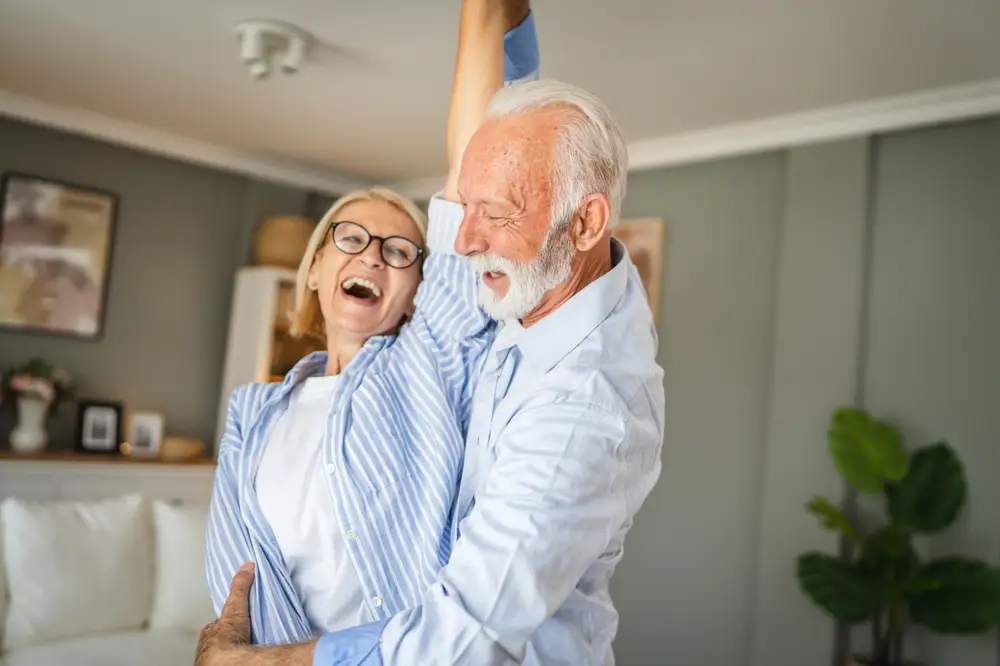 Laughing senior couple dancing together at home