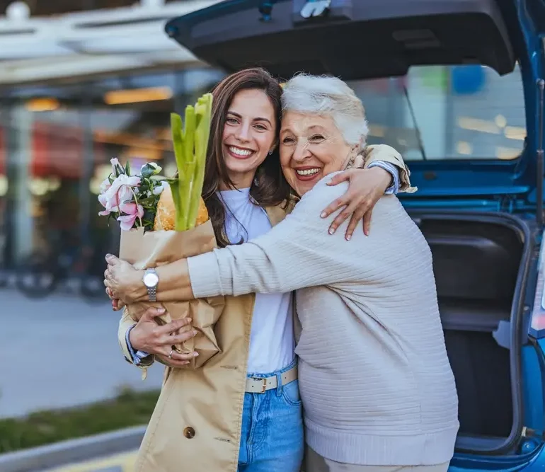 Young woman and her grandmother hugging beside a car after shopping