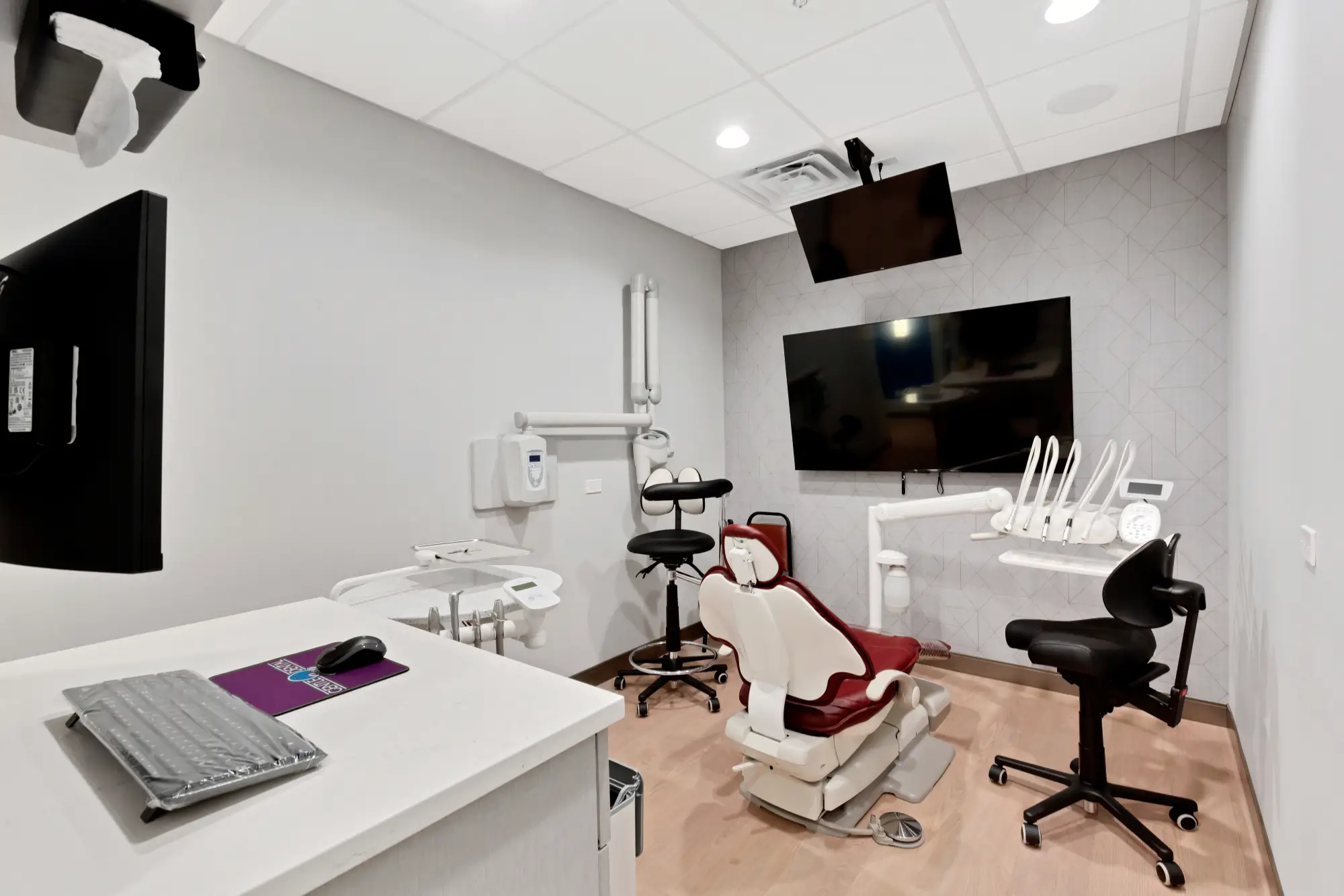 Treatment room with red dental chair, monitors and keyboard