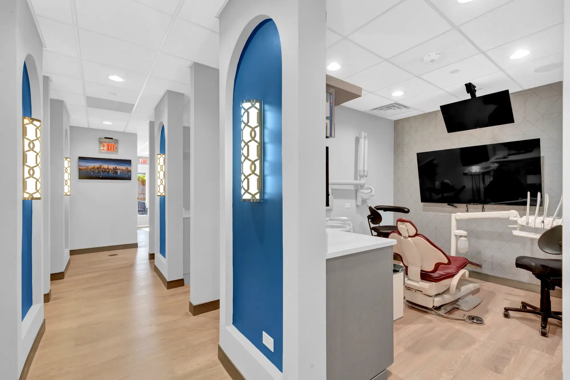 Treatment room with a red dental chair and ceiling-mounted TV