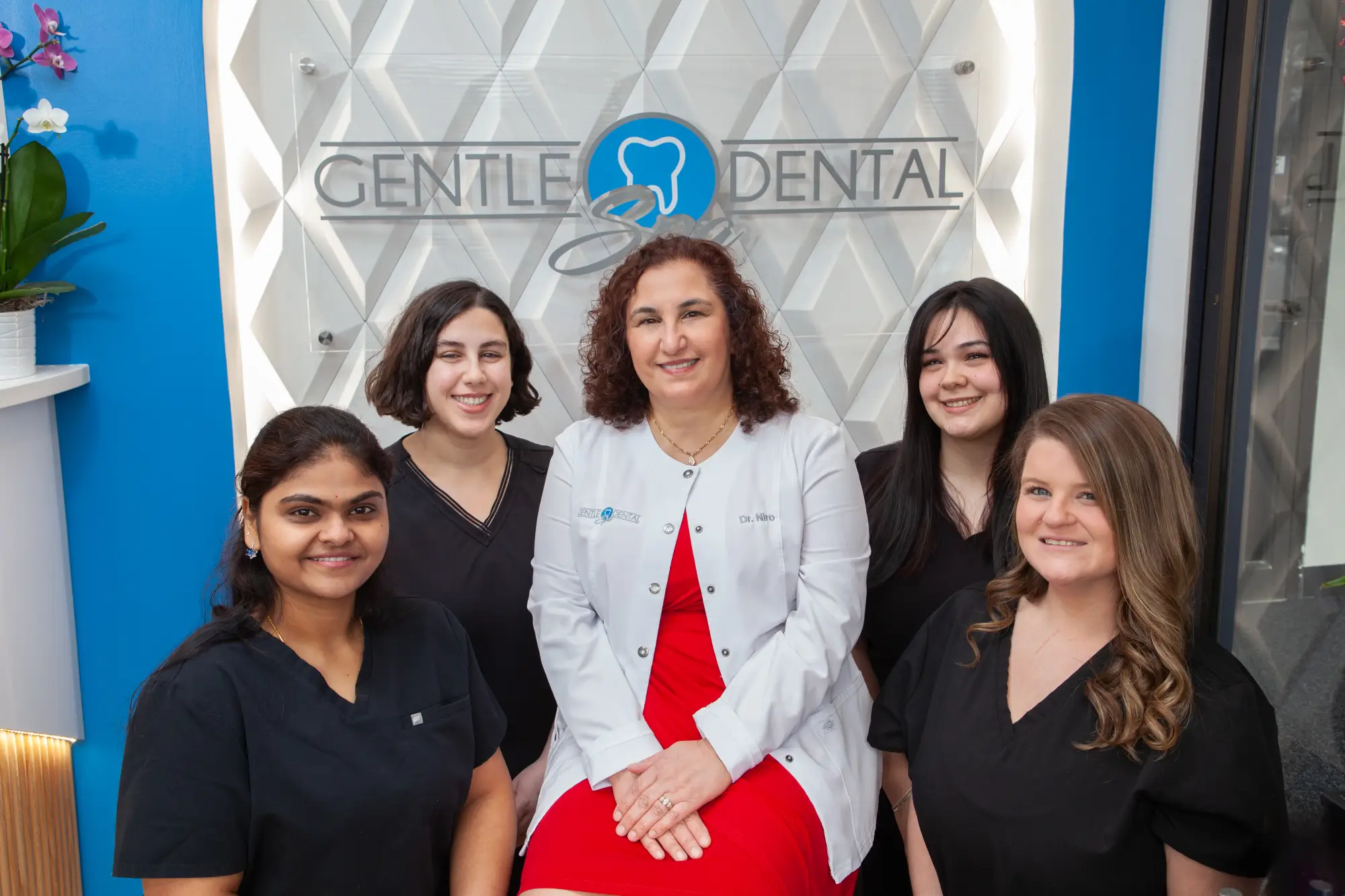 Dr. Niro-Kraemer and the Gentle Dental Spa team in front of the office logo wall